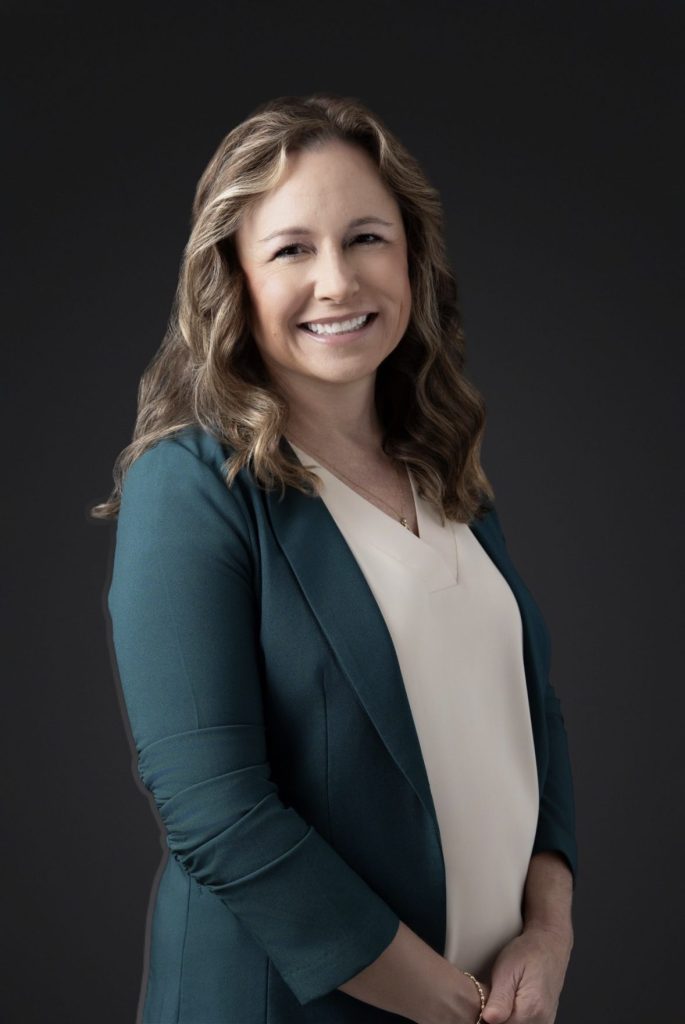 Headshot of Heather Tyre in a navy suit and a cream shirt, in front of a brown background. 