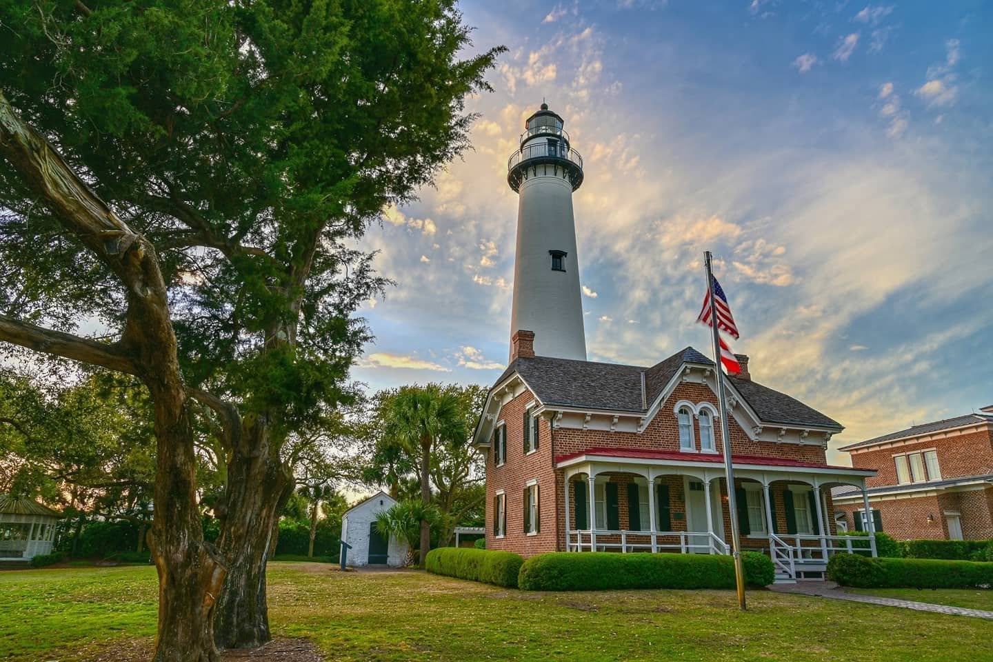 Red-gabled roof house with white and black lighthouse behind it, center of photo. 